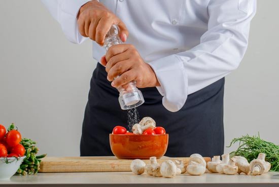 male chef adding salt into food kitchen uniform apron scaled